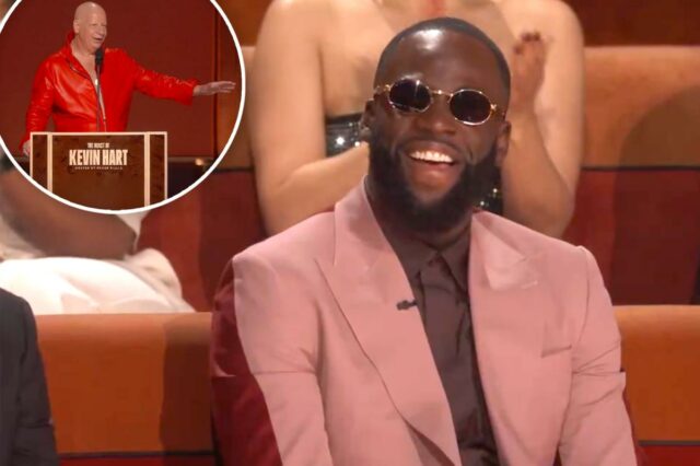 Draymond Green eviscerado por celebridades no assado de Kevin Hart: Draymond Green ri enquanto usa óculos escuros redondos e um terno rosa sobre uma camisa escura e gravata, sentado em uma cadeira vermelha.