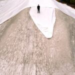 Uma foto de drone mostra uma enorme pilha de neve, camadas de lonas e um homem em pé no topo da pilha.
