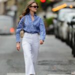 Alba Garavito Torre usa óculos escuros pretos, cabelo castanho longo e liso com uma parte central, uma blusa branca pregueada peplum sem mangas da Commense e jeans azul de cintura alta com bainha crua. Uma sandália tamanco amarela com detalhes florais da AGL é usada, combinada com um jeans jeans e uma mini bolsa Jackie marrom da Gucci. Os acessórios incluem um colar grosso com pedras naturais coloridas da Sempiterno Paris e joias de ouro. Foto de corpo inteiro, durante uma sessão de fotos de moda de rua, em 2 de maio de 2025 em Paris, França.