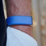 Mulher usando uma faixa de fitness Fitbit Air azul com faixas coloridas flutuando no fundo.
