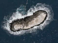 Exploradores descobrem ilha antártica desconhecida rotulada como ‘zona de perigo’ nos mapas Vista aérea de uma pequena ilha rochosa cercada por ondas em um mar azul escuro.
