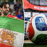 Torcedores seguram uma velha bandeira iraniana em uma partida de futebol.