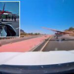 Um pequeno avião pousa em uma estrada deserta, visto do painel de um carro.