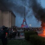 Os adeptos do PSG passam com as suas scooters pelos agentes da polícia anti-motim (traseira direita) enquanto celebram a vitória da sua equipa na final da UEFA Champions League entre o Paris Saint-Germain (PSG) e o Arsenal FC, disputada em Budapeste, na Place du Trocadero, em Paris, a 30 de maio de 2026.