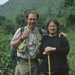 Bleddyn e Sue Wynn Jones. Sue está parada na frente de uma pedra e Bleddyn está sentado em uma