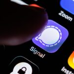 The Signal app logo can be seen on the display of a smartphone while a finger taps on the application icon.