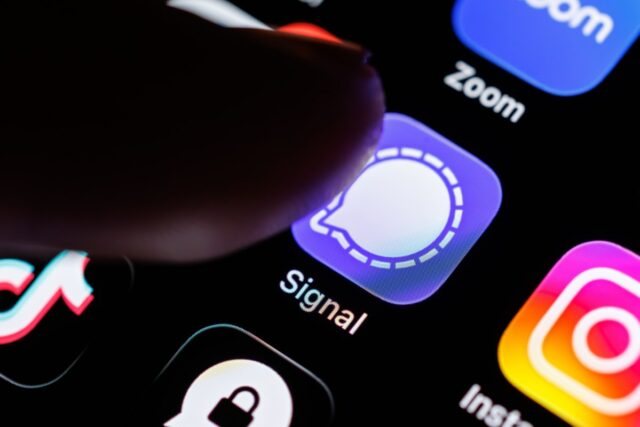 The Signal app logo can be seen on the display of a smartphone while a finger taps on the application icon.