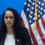 Brooke Jenkins falando em um pódio com uma bandeira americana atrás dela.