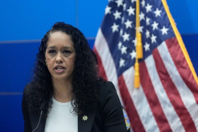 Brooke Jenkins falando em um pódio com uma bandeira americana atrás dela.