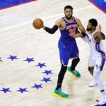 O pivô do New York Knicks, Karl-Anthony Towns (32), passa a bola enquanto o atacante do Philadelphia 76ers, Paul George (8), defende.