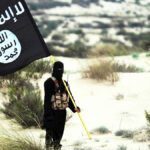 Combatente mascarado do Estado Islâmico segura bandeira do ISIS no deserto