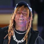 Lil Wayne sorrindo, usando um boné preto, dreadlocks, duas correntes de diamantes e uma grelha.