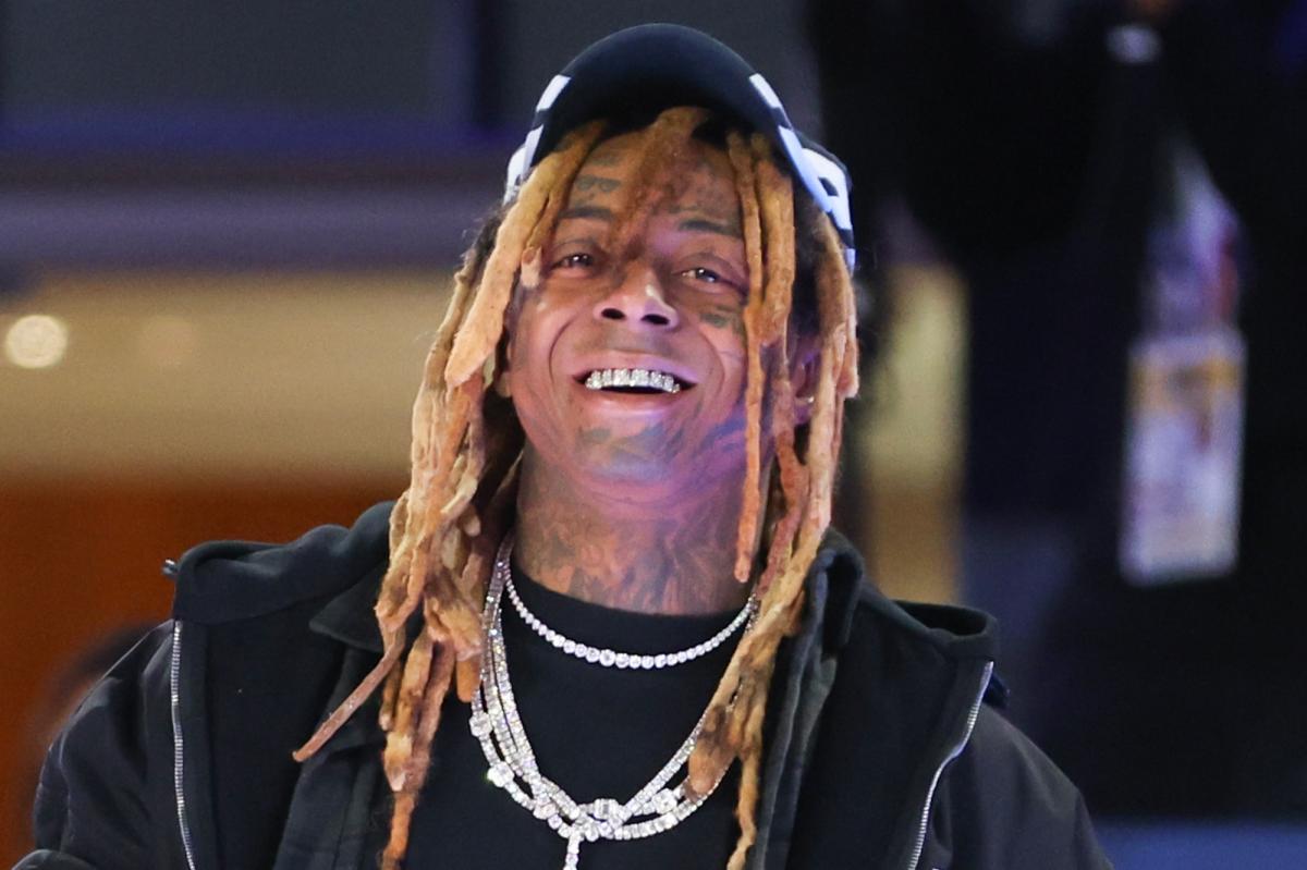 Lil Wayne sorrindo, usando um boné preto, dreadlocks, duas correntes de diamantes e uma grelha.