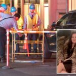 Trabalhadores inspecionam o local de um acidente onde uma mulher caiu em um bueiro descoberto ao lado de um SUV Mercedes-Benz preto.