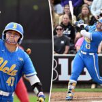 Uma jogadora de softball da UCLA com uniforme azul e capacete levantando a mão enluvada no ar.