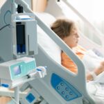 A stock image of a sick child in a hospital room with an oxygen tube and IV line.
