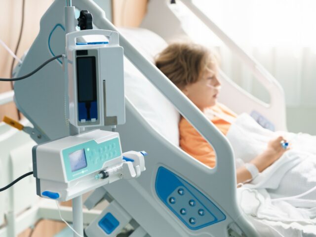 A stock image of a sick child in a hospital room with an oxygen tube and IV line.