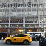 Um homem segura um smartphone em frente ao prédio do New York Times.