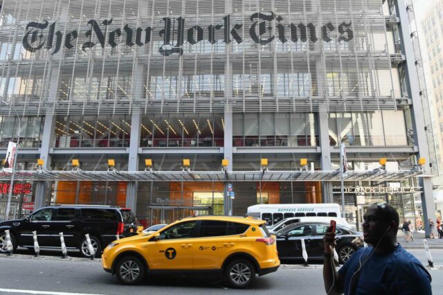 Um homem segura um smartphone em frente ao prédio do New York Times.