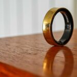 Um Samsung Galaxy Ring dourado apoiado verticalmente na borda de uma mesa de madeira