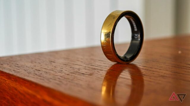Um Samsung Galaxy Ring dourado apoiado verticalmente na borda de uma mesa de madeira