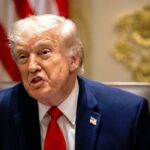 Donald Trump, vestindo terno escuro, camisa branca e gravata vermelha com um distintivo de lapela com a bandeira americana, discursa em uma reunião de gabinete.