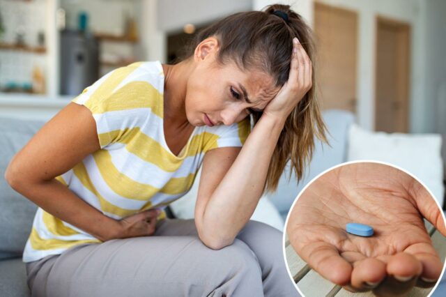 O Viagra pode ajudar com um problema que atinge até Mulher sentada em um sofá, segurando a cabeça e o estômago com dor, sofrendo de enxaqueca e cólicas abdominais.