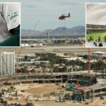 Canteiro de obras de um novo estádio em Las Vegas, com um helicóptero sobrevoando, um hotel em primeiro plano e um aeroporto com montanhas ao fundo.