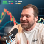 O cofundador da DraftKings, Matt Kalish, falando ao microfone discutindo os mercados de previsão com gráficos de negociação de ações atrás dele durante uma entrevista na indústria de apostas esportivas. O cofundador da DraftKings critica os mercados de previsão de Kalshi em meio às crescentes tensões na indústria de apostas esportivas