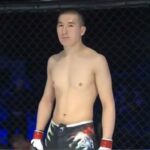 Medet Zheenaliev, sem camisa e usando shorts e luvas de luta, em uma jaula de combate.