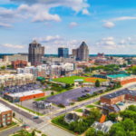 Vista aérea do centro de Greensboro, Carolina do Norte, apresentando o horizonte da cidade, o estádio de beisebol, edifícios comerciais e bairros vizinhos. O novo site do Lumbee explica a próxima alteração na votação dos jogos tribais antes de junho