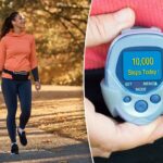 Uma mulher atlética feliz com fones de ouvido, um moletom com capuz laranja e leggings escuras caminha por um parque de outono.
