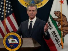 O orçamento de Gavin Newsom ignora a bomba-relógio fiscal da Califórnia Gavin Newsom falando em um pódio com as bandeiras dos EUA e da Califórnia atrás dele.