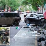 Um policial cuida de um homem de agasalho vermelho e branco deitado na calçada ao lado de um SUV preto danificado e de bicicletas, cercado por outros policiais e curiosos.
