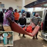 Pessoas carregam um paciente em uma maca até uma ambulância enquanto outros observam do lado de fora de um prédio com um