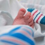 Um close dos dedinhos dos pés de um bebê enrolados em um cobertor listrado de branco e azul.