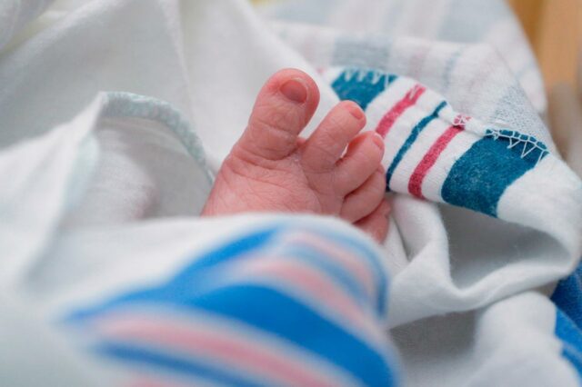 Um close dos dedinhos dos pés de um bebê enrolados em um cobertor listrado de branco e azul.