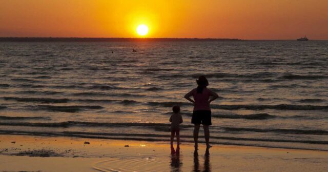 Uma mulher e uma criança observam o pôr do sol na praia de Mindil, em Darwin.