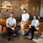 Two men and a woman sit on leather chairs in a well appointed office space.