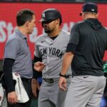 Jasson Dominguez, do New York Yankees, ao centro, conversa com um treinador do time enquanto o técnico Aaron Boone, à direita, observa depois que Dominguez foi atingido por um arremesso no quarto turno de um jogo de beisebol contra o Texas Rangers na quarta-feira, 29 de abril de 2026, em Arlington, Texas.
