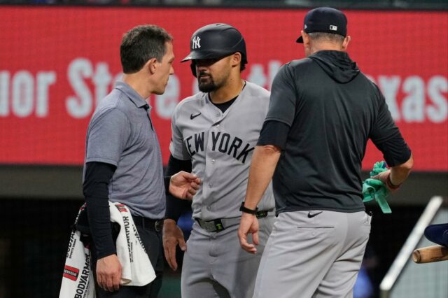 Jasson Dominguez, do New York Yankees, ao centro, conversa com um treinador do time enquanto o técnico Aaron Boone, à direita, observa depois que Dominguez foi atingido por um arremesso no quarto turno de um jogo de beisebol contra o Texas Rangers na quarta-feira, 29 de abril de 2026, em Arlington, Texas. 