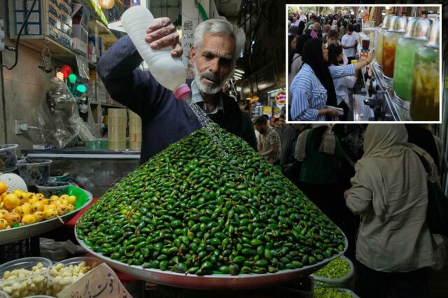 Um vendedor de frutas regando amêndoas verdes em um mercado.