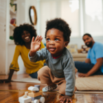 A stock photo showing a child playing a game with a train toy while his parents are laughing from the background.