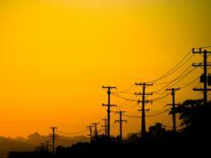 Os preços da energia subiram 76% na maior rede da América, e um cão de guarda está apontando o dedo Power lines and trees in California at sunset.
