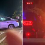 Carro branco com manchas de sangue nas laterais em um estacionamento à noite, com pessoas e árvores ao fundo.