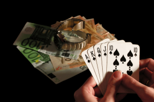 Pesquisadores universitários lançam um grande centro independente de evidências de Pessoa segurando a mão de pôquer royal flush ao lado de notas de euro e relógio de luxo simbolizando ganhos em jogos de azar, apostas em cassinos e risco financeiro. Pesquisadores universitários lançam um grande centro independente de evidências de danos ao jogo no Reino Unido
