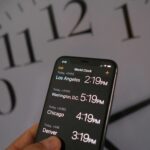 This illustration photo shows a clock in the background of a smartphone showing the time.