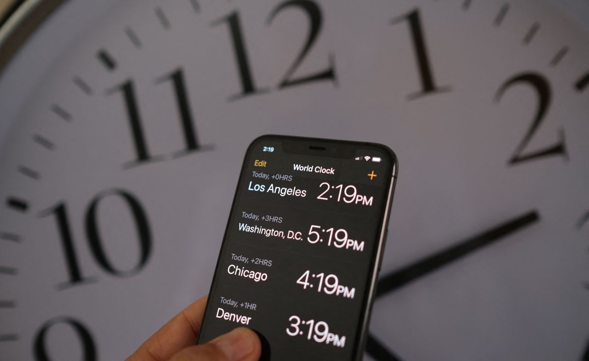 This illustration photo shows a clock in the background of a smartphone showing the time.