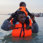 Quase 400 migrantes chegaram ontem ao Reino Unido em seis pequenos barcos, enquanto gangues de tráfico de pessoas aproveitavam o tempo quente. Na foto: Um migrante carregando uma criança no mar, espera para embarcar em um barco inflável na praia de Dunquerque