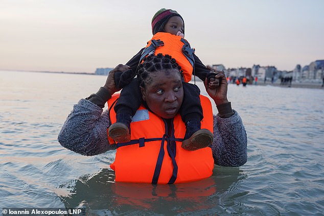 Quase 400 migrantes chegaram ontem ao Reino Unido em seis Quase 400 migrantes chegaram ontem ao Reino Unido em seis pequenos barcos, enquanto gangues de tráfico de pessoas aproveitavam o tempo quente. Na foto: Um migrante carregando uma criança no mar, espera para embarcar em um barco inflável na praia de Dunquerque